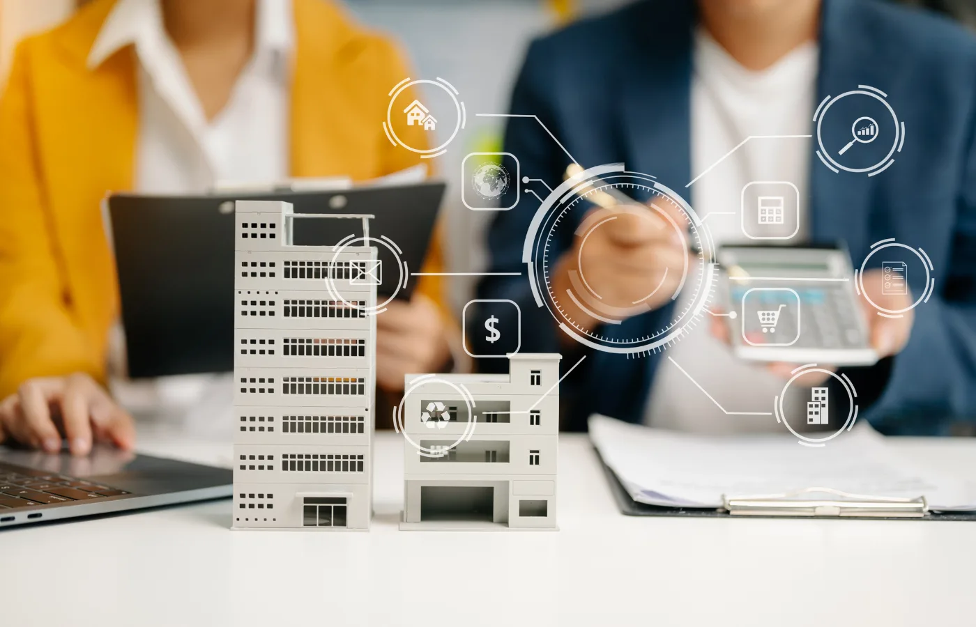Integrated BMS (Building Management System) concept image showing miniature commercial buildings on a desk with digital interface icons representing energy management, security, finance, and smart building operations, symbolising centralized control and intelligent facility management in modern workplaces.